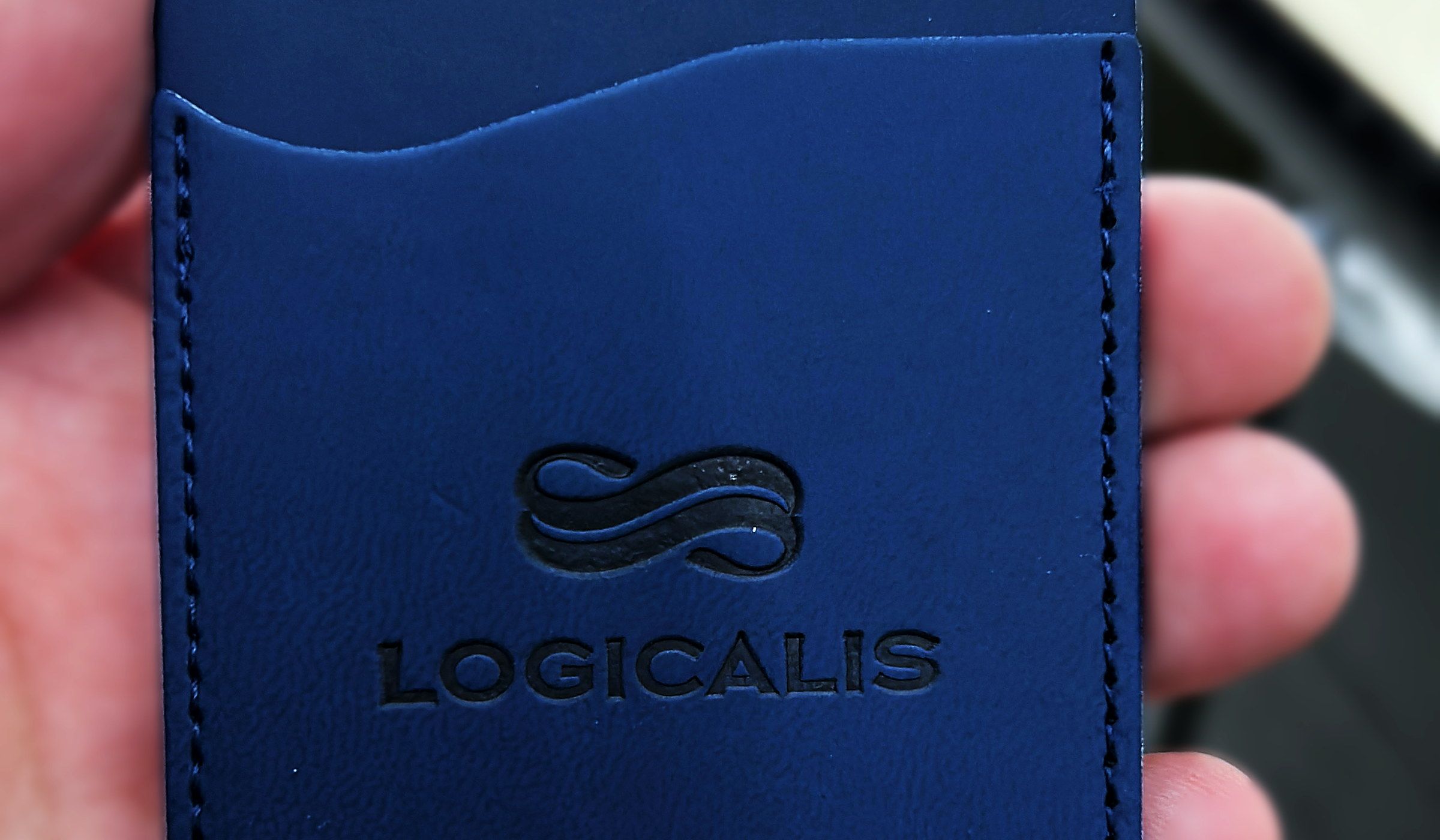 Porta-cartões de couro azul com a marca Logicalis prensada em baixo-relevo, seguro na mão